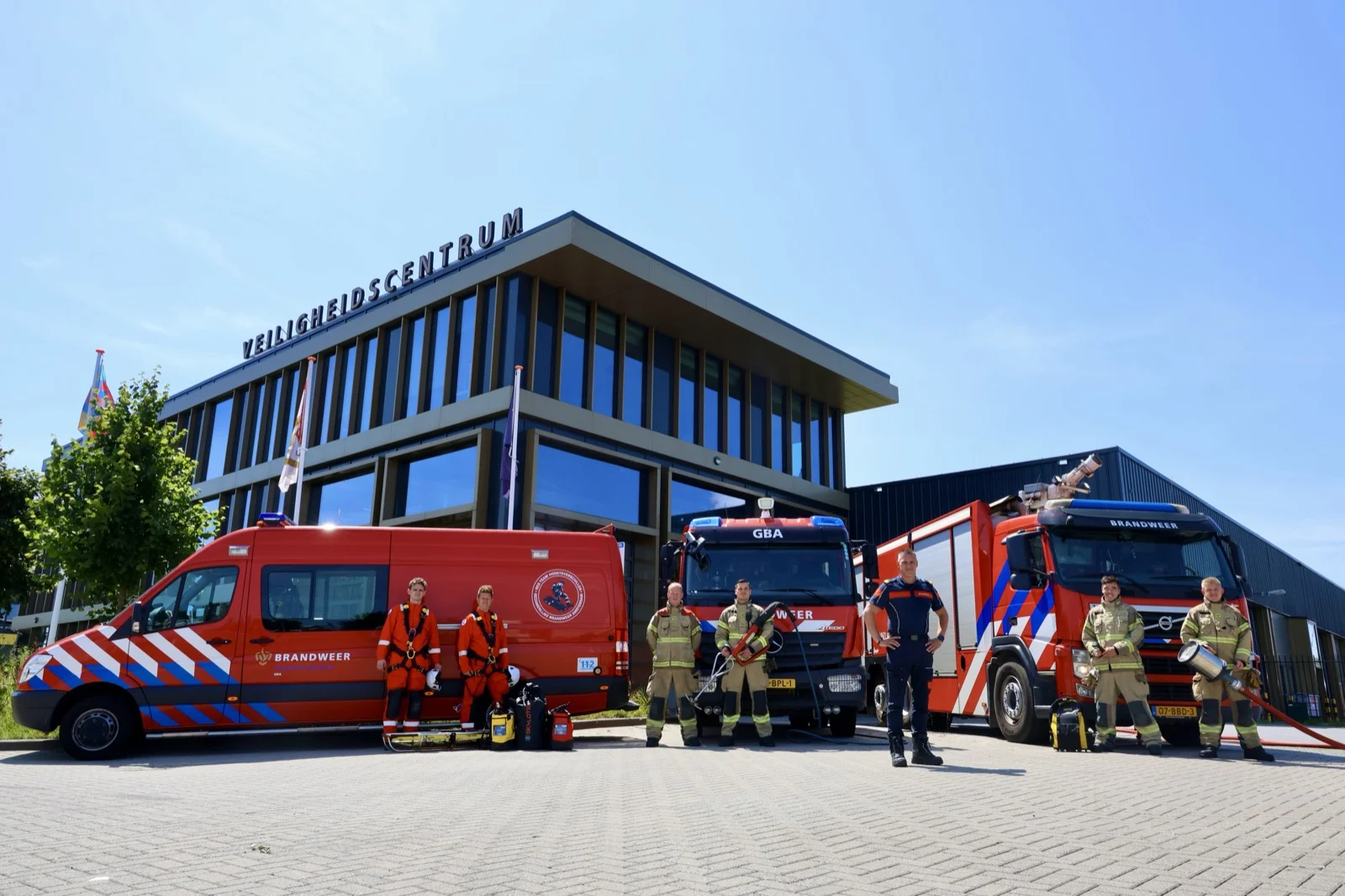 Het Veiligheidscentrum waar de GBA gevestigd is &mdash; brandweer- en GBA-voertuigen voor het pand, een groep brandweer in tenue ervoor.